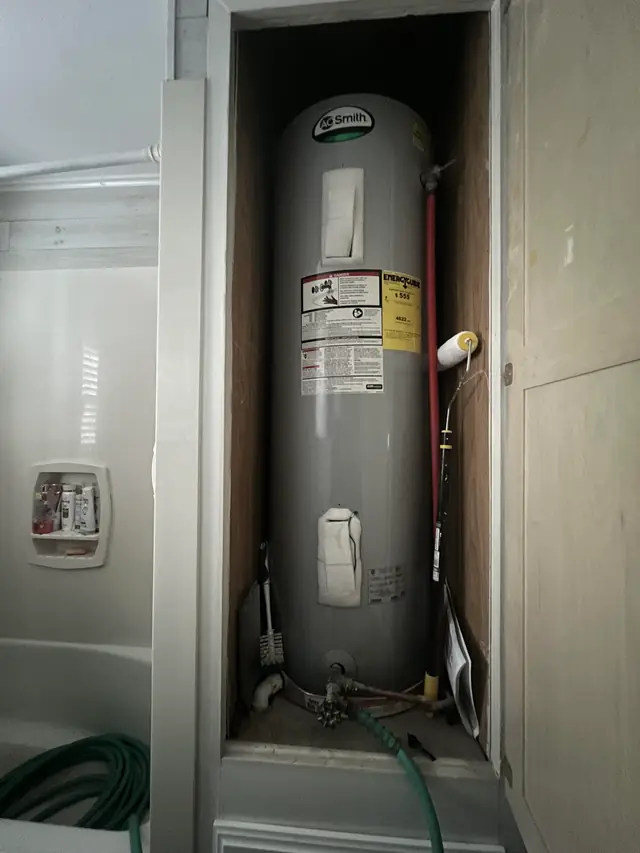 A new electric water heater installed in a white hallway closet with a drain hose attached