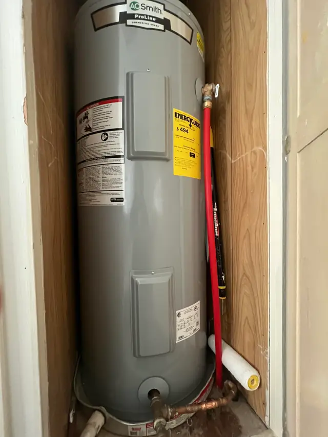 A tall electric water heater standing in a wood-lined closet, red relief line down its side