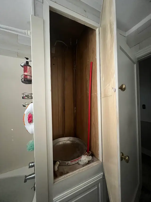 An empty water heater closet with the old tank removed and the drain pan left on the floor
