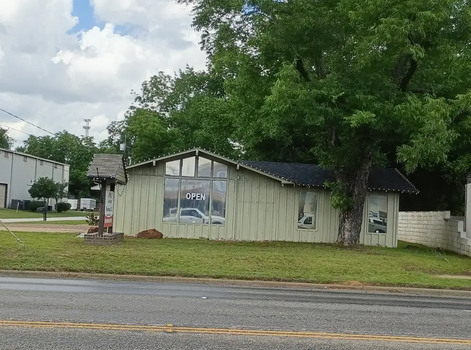 The Artesian Plumbing shop on W 2nd St in Chandler, a pale green board-and-batten building with a large tree in front